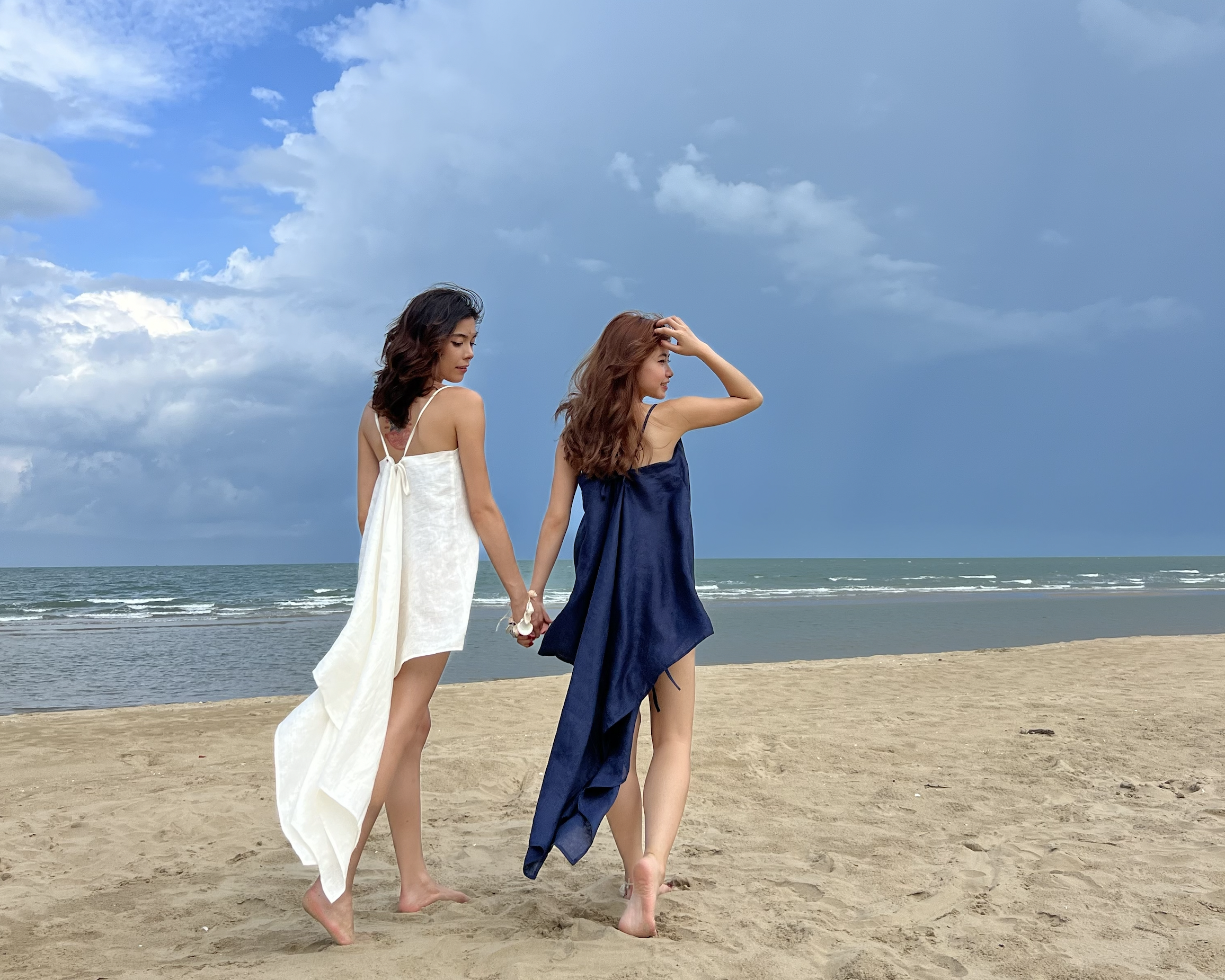 Two women standing in flowing dresses on a beach